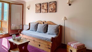 A cozy room with a wooden sofa, a small table, and a bench. There are wall-mounted lamps and a mirror.