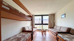 Una habitación con literas, un sofá, una mesita y vistas a las montañas a través de una ventana.