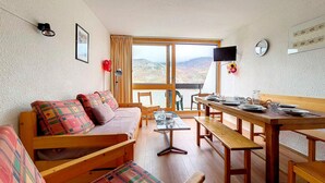 Una habitación acogedora con sofá, bancos de madera, una mesa lista para comer, televisión y vistas al exterior.