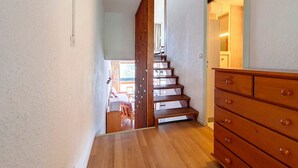 Una escalera de madera que lleva al segundo piso, un aparador de madera con cajones, y vistas a un comedor con una mesa y sillas.