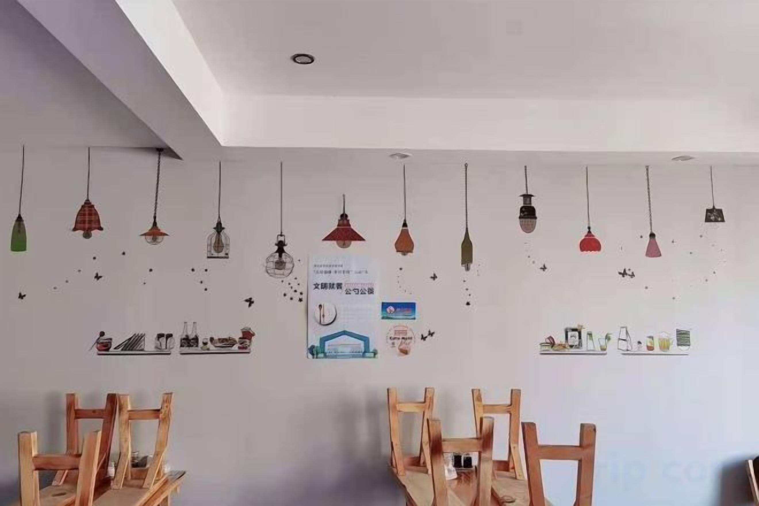 Een kamer met houten stoelen, hangende吊灯 en wanddecoraties, waaronder een poster en kleine plankjes.