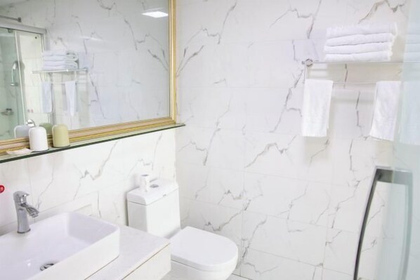A bathroom with a marble wall, a glass shower enclosure, a white sink, and a toilet. - Tianzihu Boutique Hotel (Anji)