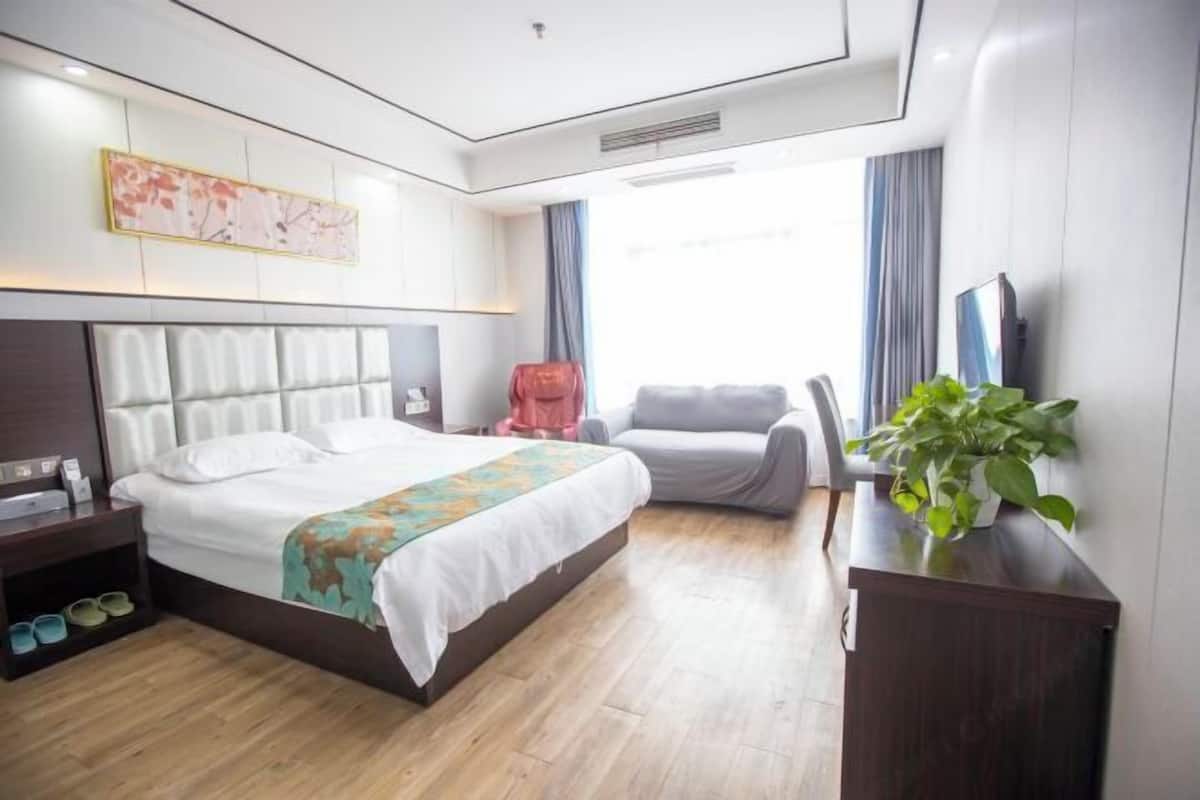 A modern hotel room with a large bed, a desk, a chair, and a plant.
