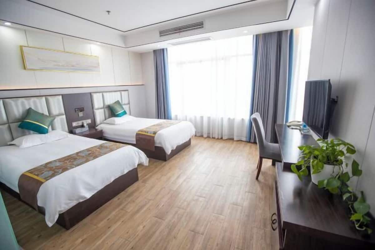 A hotel room with two beds, a desk, a chair, and a television.