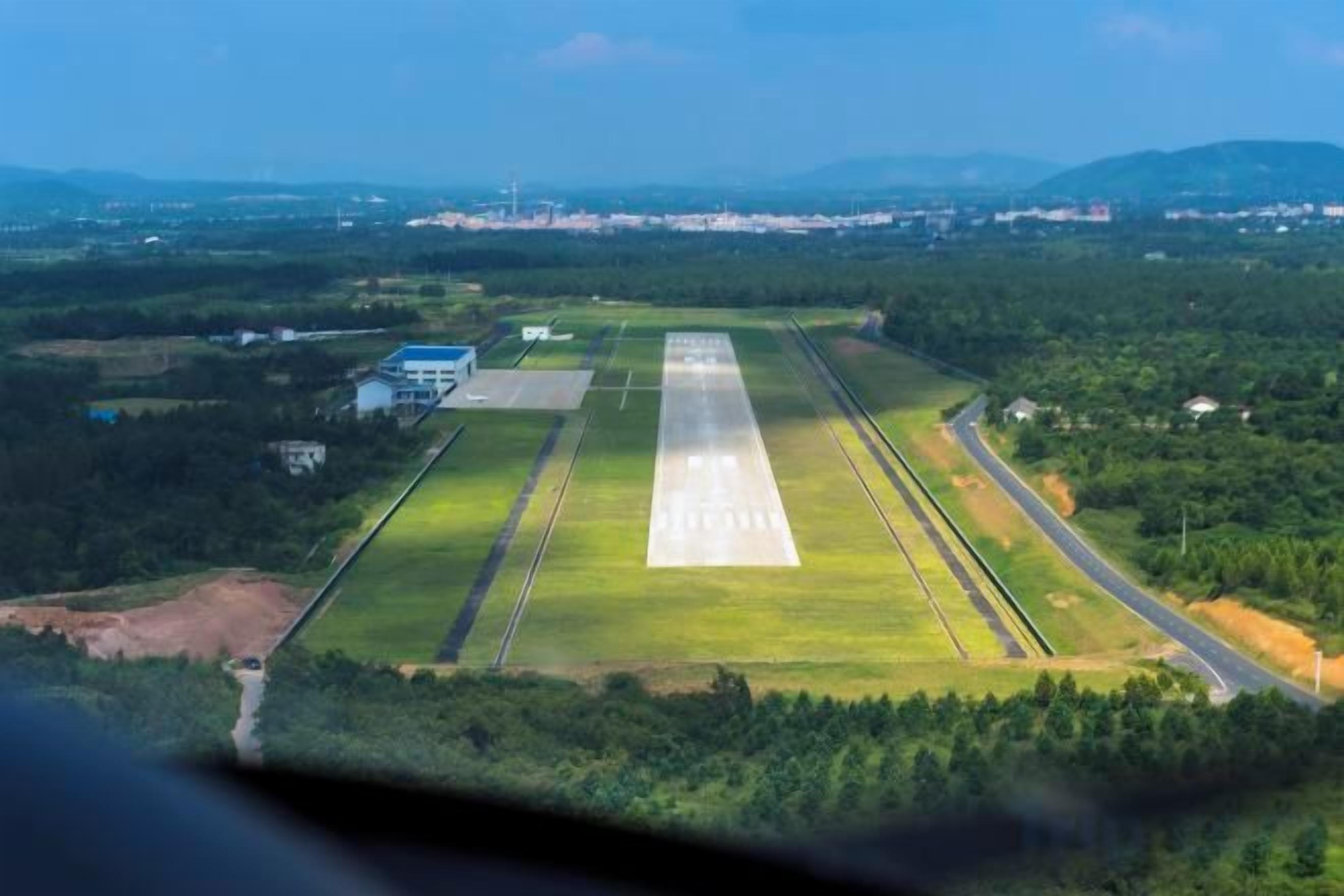 Eine Startbahn mit umgebender Vegetation und Gebäuden in der Ferne.