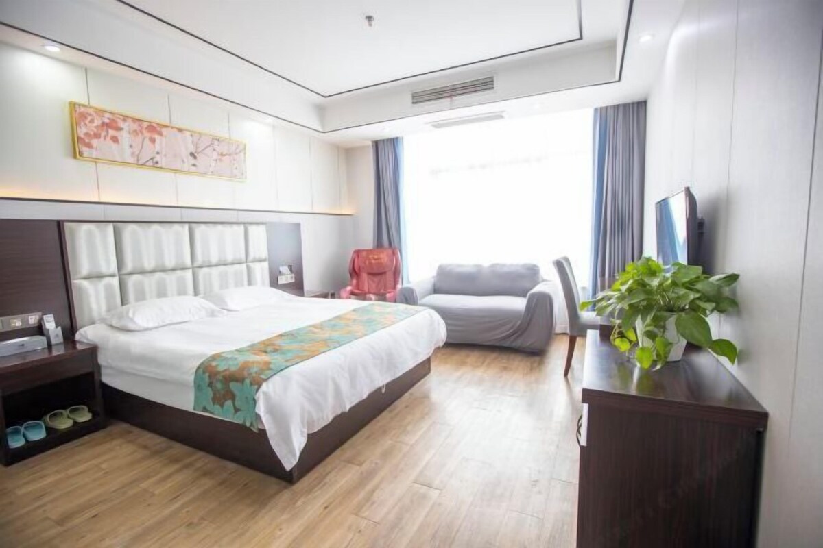 A hotel room with a bed, a desk, a chair, a TV, and a plant.