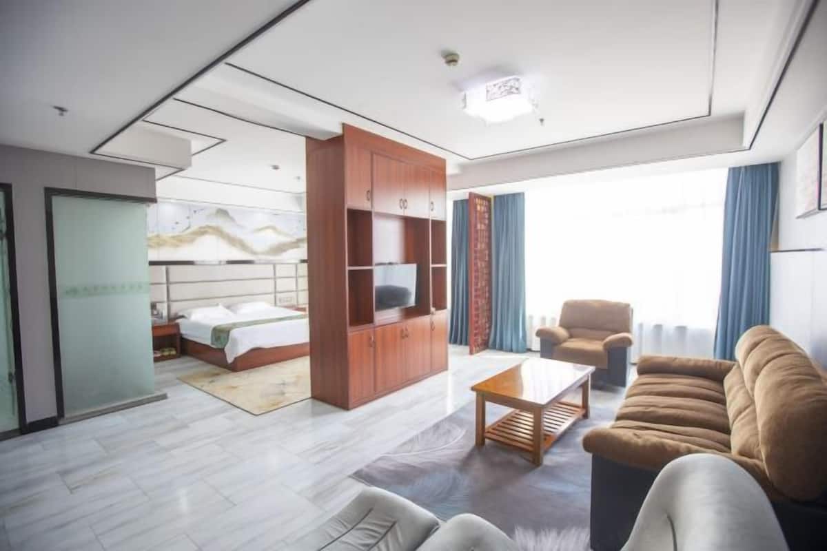 A modern hotel room with a bed, a wooden cabinet with a TV, a sofa, and a coffee table.
