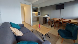 Una sala de estar moderna con un sofá, una mesa de centro y un comedor con sillas. Se ve una cocina al fondo.