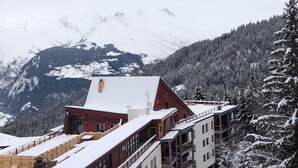 Un edificio de varios pisos con fachada roja y techo cubierto de nieve, rodeado de árboles y montañas nevadas.