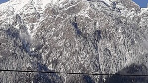 Una montaña nevada con una cruz en la cima, rodeada de árboles.