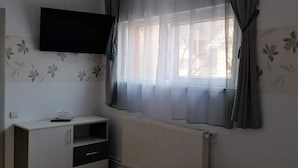 Un dormitorio con cama, televisión montada en la pared, radiador y ventana con cortinas.