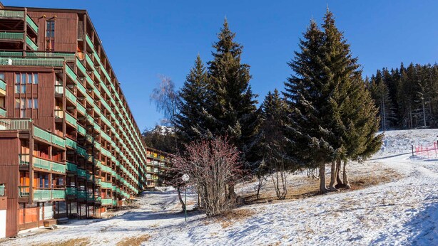 Un hôtel à plusieurs étages doté de balcons, entouré d’un paysage enneigé et d’arbres à feuilles persistantes.
