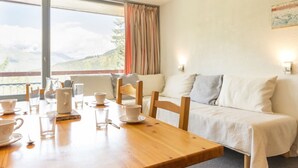 Une pièce avec une table en bois mise pour le thé, un canapé et une vue sur les montagnes à travers de grandes fenêtres.
