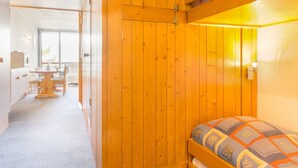 Une pièce aménagée comme un chalet en bois, avec un lit superposé, une petite kitchenette et un coin repas comprenant une table et des chaises.