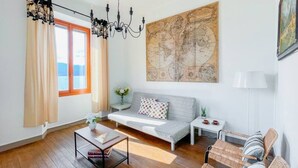 Un salon moderne avec un canapé, une table basse, des fauteuils en osier, une carte accrochée au mur et une fenêtre avec des rideaux.