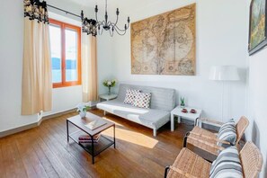 Ein modernes Wohnzimmer mit einer Couch, einem Couchtisch, Korbstühlen, einer Karte an der Wand und einem Fenster mit Vorhängen.