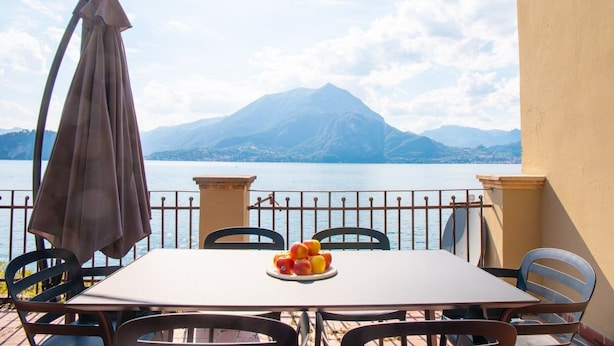 Une table entourée de chaises, recouverte d’une nappe, sur un balcon donnant sur un lac et des montagnes.