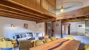 A cozy living room with a wooden ceiling, a dining table, and yellow chairs.