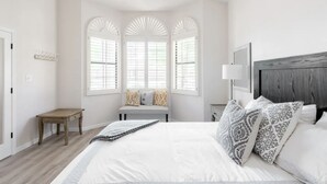 A bedroom with a large bed, a nightstand, a bench, and a window with shutters.