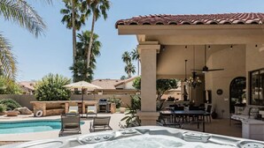A hot tub with a pool, outdoor seating, and a patio area with a pergola.