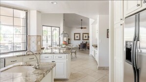 A spacious kitchen with a large island, white cabinetry, and a stainless steel refrigerator.