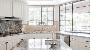 A modern kitchen with white cabinets, a granite countertop, a built-in stove, and a large window with a view of greenery.
