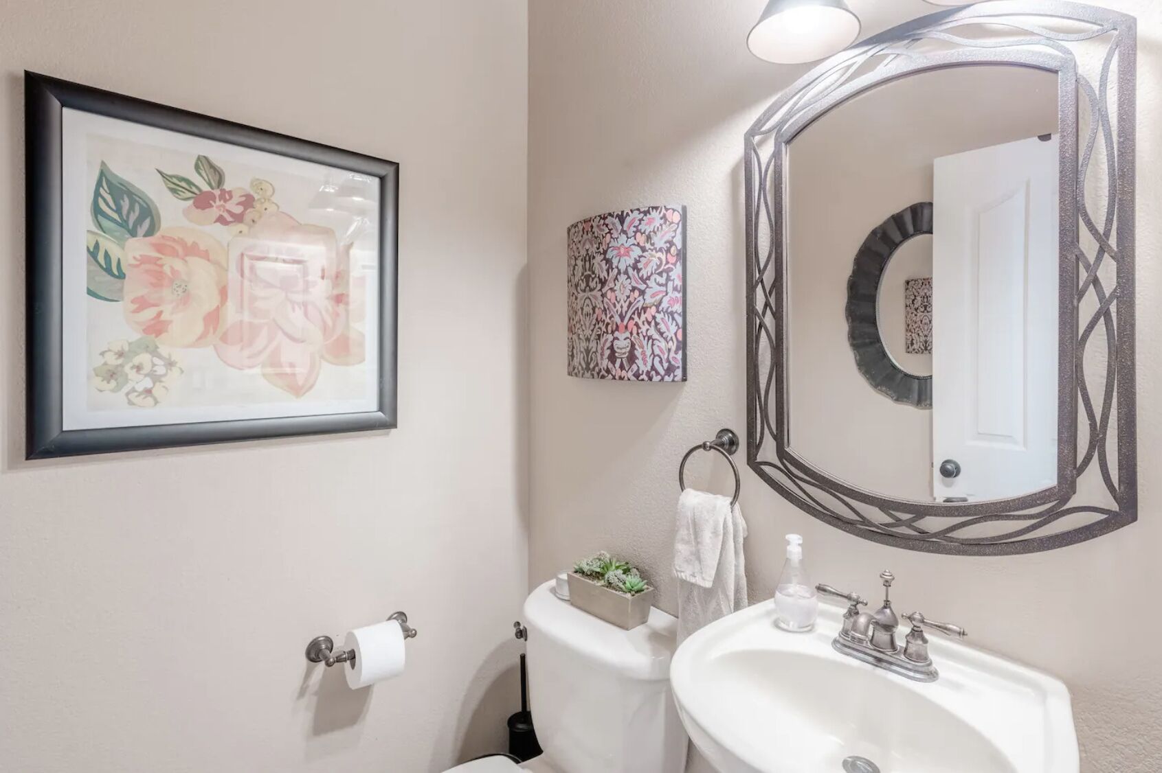 A bathroom with a toilet, sink, framed floral artwork, and a decorative mirror.