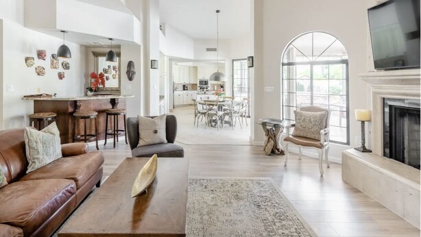 A spacious living room with a brown leather sofa, a wooden coffee table, and a fireplace. There is a dining area with a table and chairs, and a kitchen in the background.
