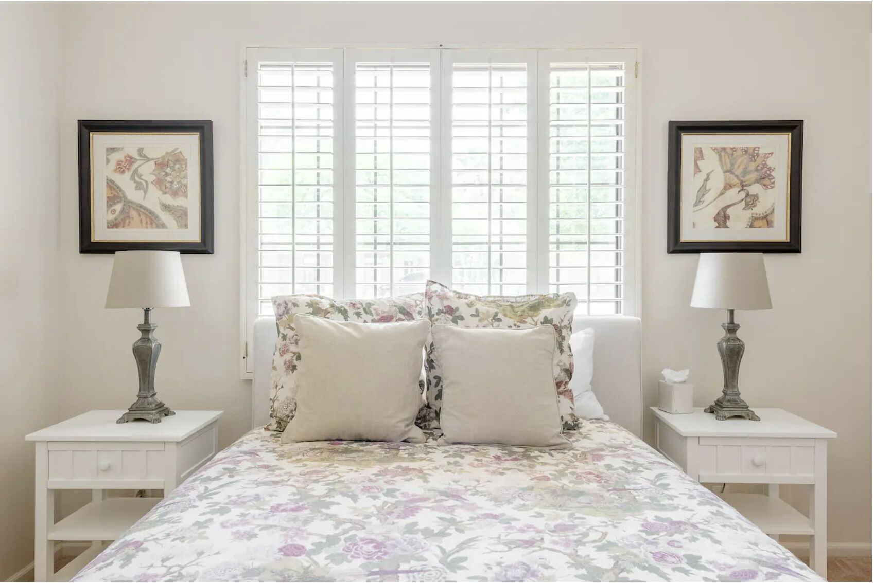 A bedroom with a floral bedspread, two bedside tables with lamps, and framed artwork on the walls.