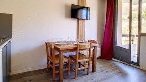 Zona pranzo con tavolo in legno apparecchiato per due persone, televisore a parete e una porta vetrata scorrevole che dà su un'area esterna.