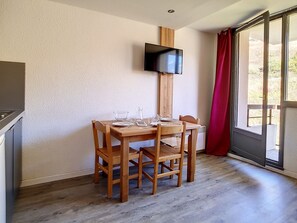 Un comedor con una mesa de madera dispuesta para dos, un televisor montado en la pared y un divisor corredizo de vidrio que da a un espacio exterior.