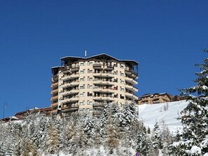 Un hotel de varios pisos con balcones, rodeado de árboles nevados y un cielo azul despejado.