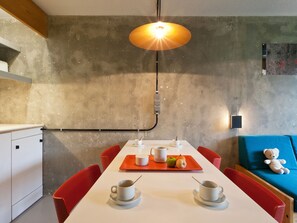A modern dining area with a white table, red chairs, and a hanging light fixture.