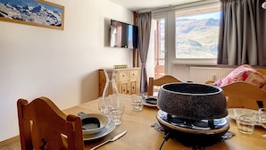 Un comedor con una mesa preparada para dos personas, un televisor montado en la pared y una ventana con vistas a las montañas.