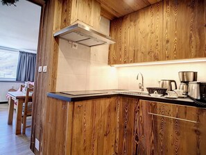 Moderni keittiö, jossa on puiset kaapit, ruostumattomasta teräksestä valmistettu liesituuletin sekä työtaso, jossa on pesuallas ja kahvinkeitin.