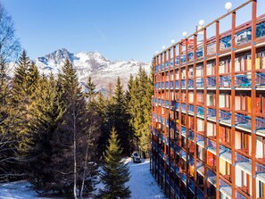 Un edificio de varios pisos con nieve en el suelo y una montaña al fondo.