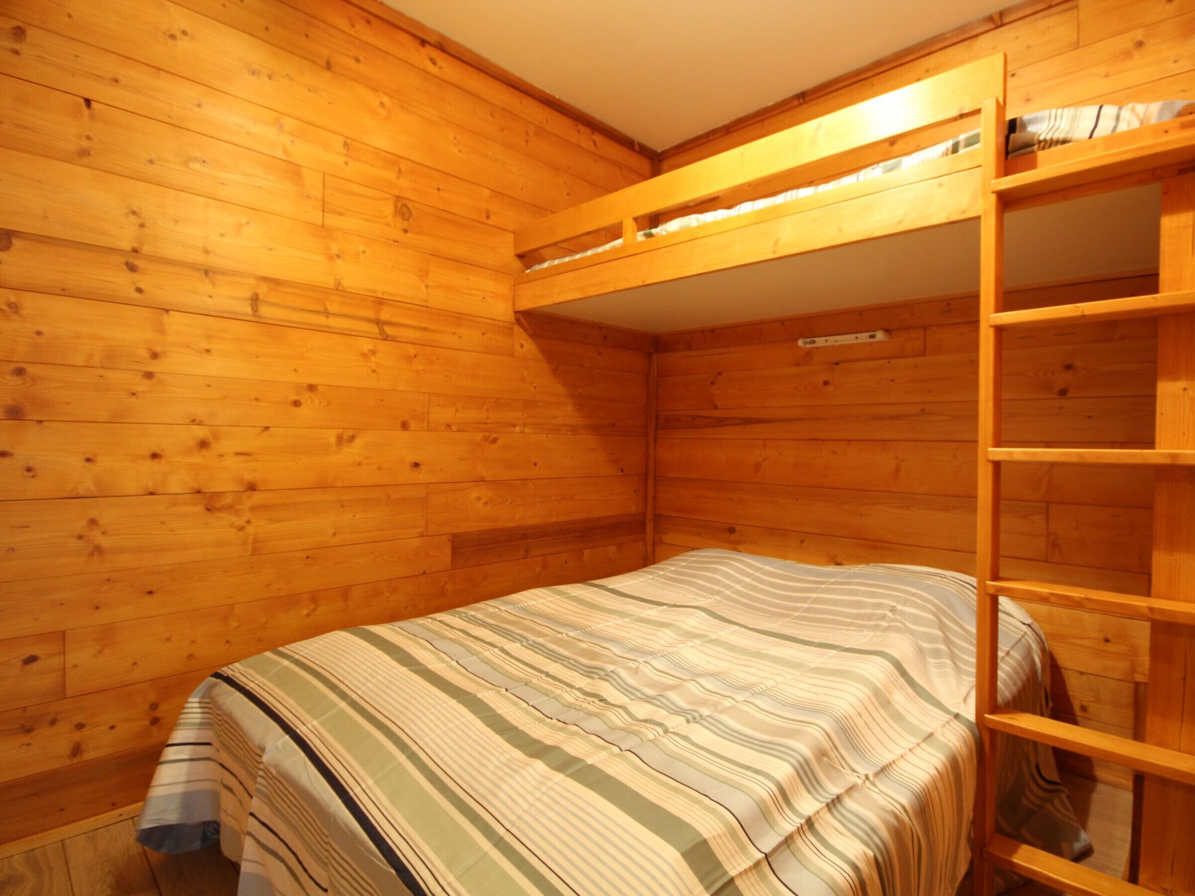 A small, wooden cabin room with a bunk bed and a wooden ladder.