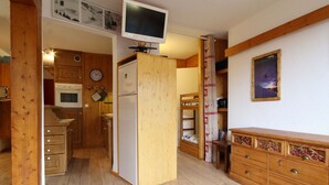 Eine kleine Küche mit Holzausstattung, einer Mikrowelle, einem Kühlschrank und einem an der Wand befestigten Fernseher.