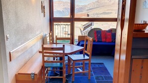 Une pièce chaleureuse avec une table et des chaises en bois, un banc et une vue sur les montagnes, visible à travers de grandes fenêtres.