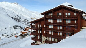 A multi-story wooden building with balconies, surrounded by snow-covered mountains. - 2-room apartment · Ski-in/Ski-out · Southwest balcony (Les Menuires)