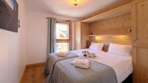 A cozy bedroom with two beds, wooden headboard, a window with curtains, and a bedside table with a lamp. - Spacious chalet with sauna, slope access, Wi-Fi and parking (Saint-Martin-de-Belleville)