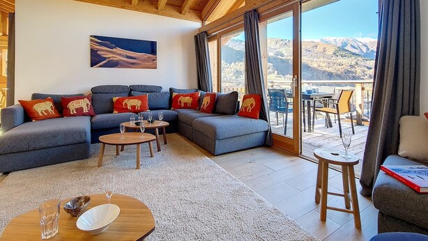 A modern living room with a large sofa, a coffee table, and a view of mountains through large windows. - Spacious chalet with sauna, slope access, Wi-Fi and parking (Saint-Martin-de-Belleville)