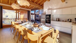 A modern kitchen with white cabinets and stainless steel appliances, a dining area with wooden tables and chairs, and a balcony with a view of the mountains. - Spacious chalet with sauna, slope access, Wi-Fi and parking (Saint-Martin-de-Belleville)