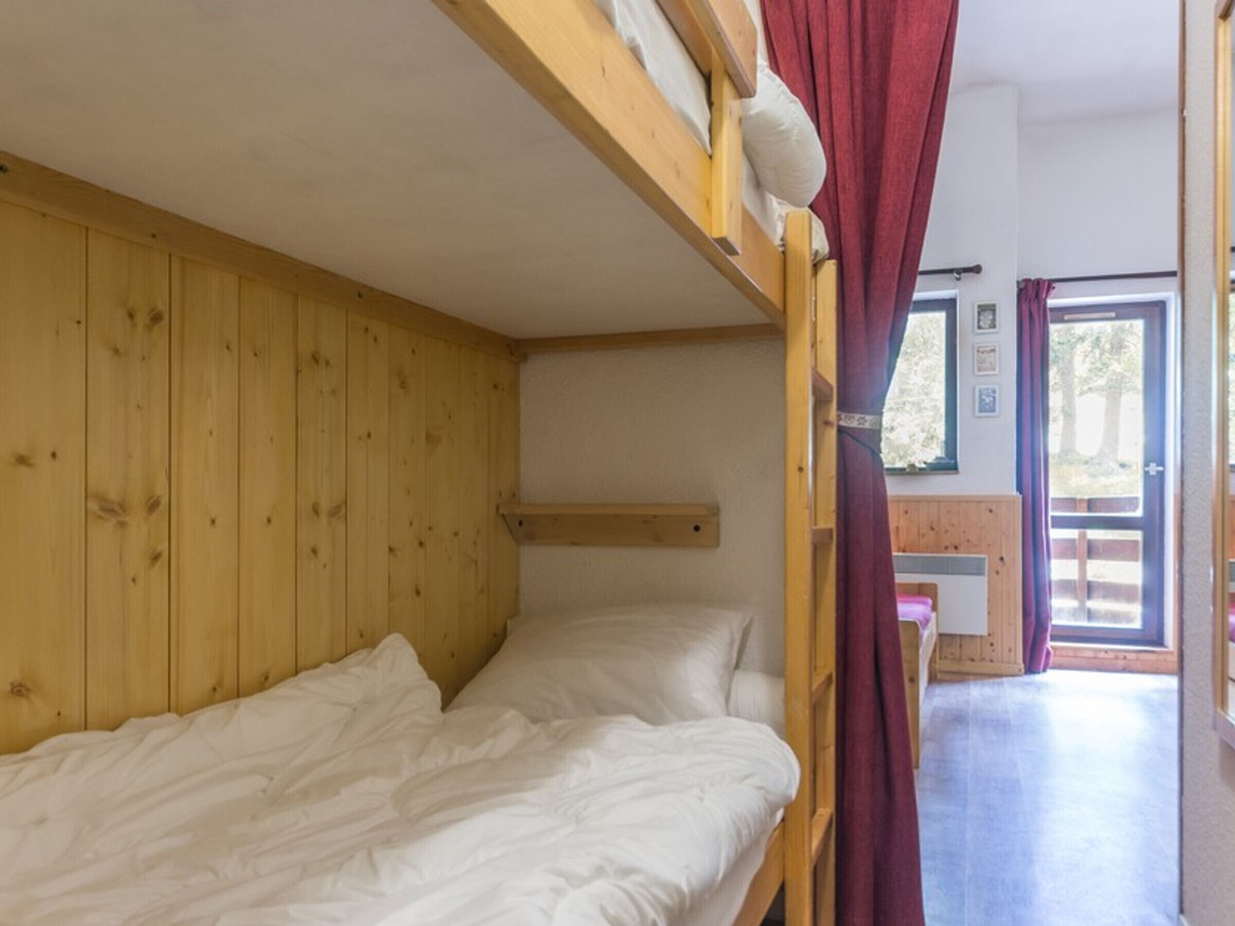 A bunk bed room with wooden walls, a small shelf, and a door leading to an outdoor area.
