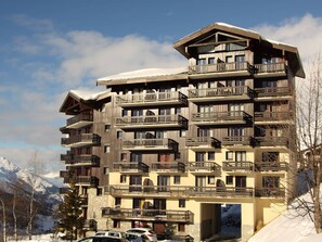 A multi-story hotel with balconies, a stone base, and a snowy mountain backdrop.