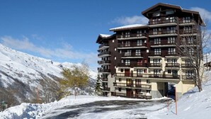 A multi-story hotel with balconies, set against a snowy mountain backdrop.