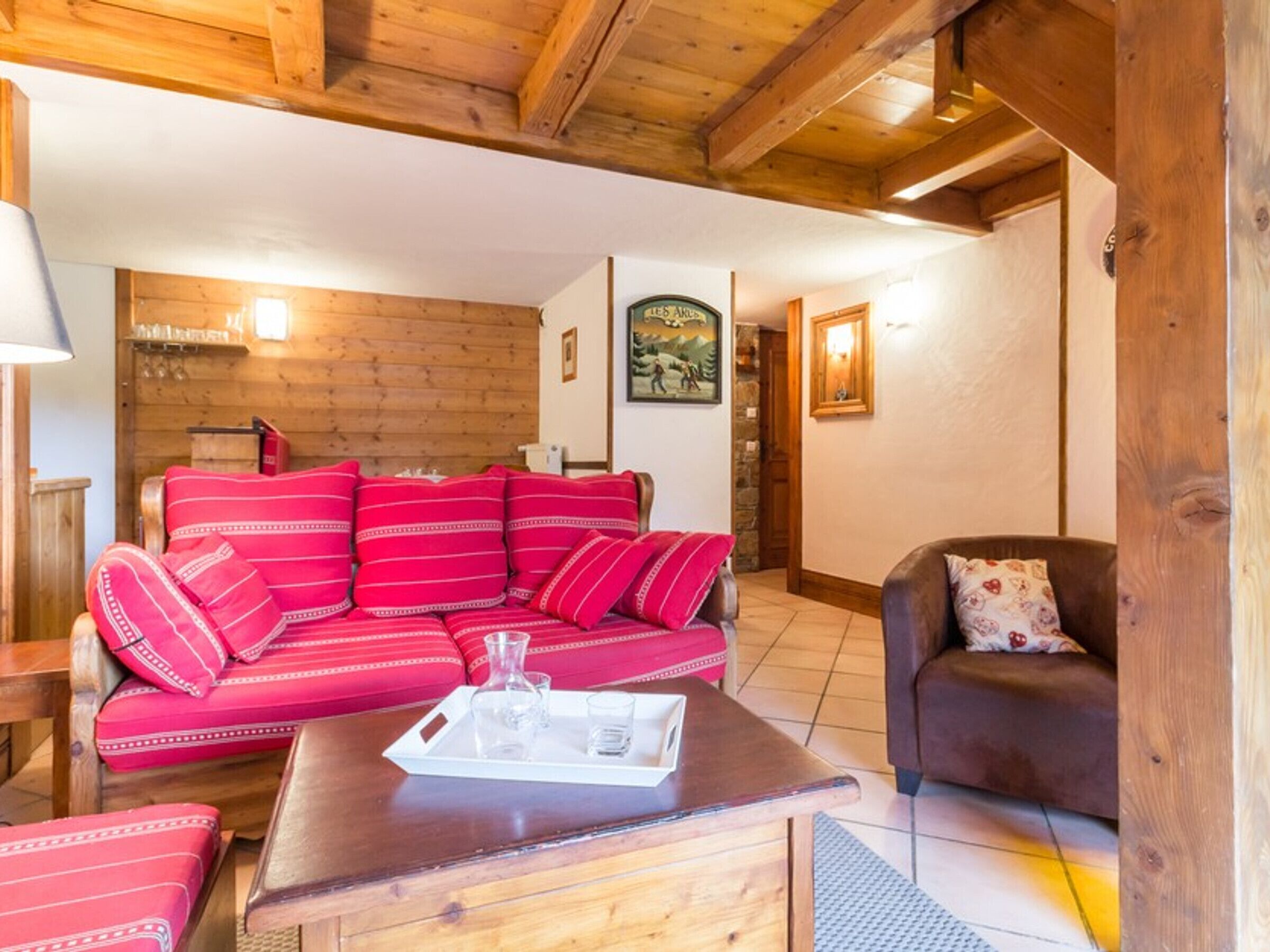 Un accogliente soggiorno con soffitto in legno, un divano rosso con motivo decorativo, un divano marrone e un tavolino in legno con vassoio.