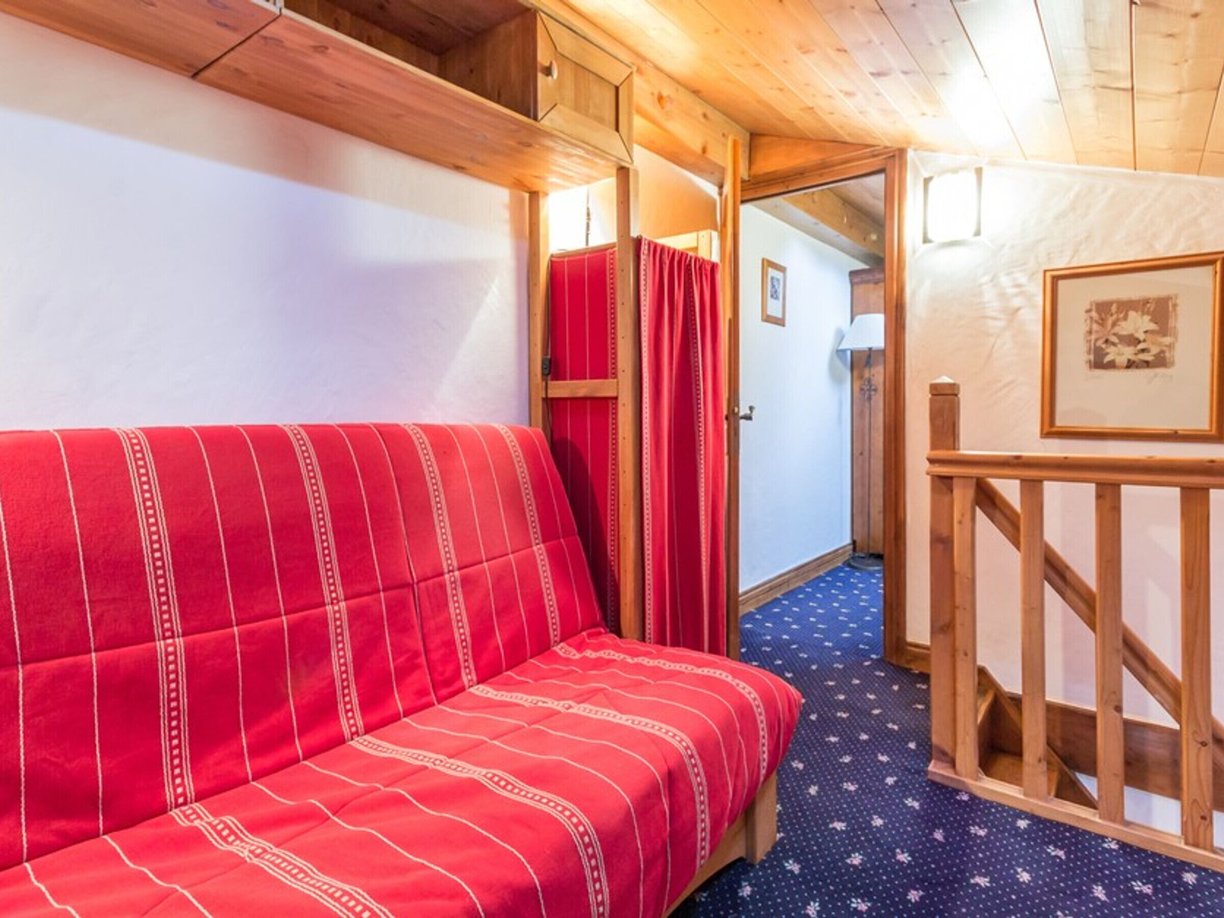 Ein gemütliches Zimmer mit einem rotgestreiften Sofa, Holzbalken an der Decke, einer Holztreppe und einem gerahmten Bild an der Wand.