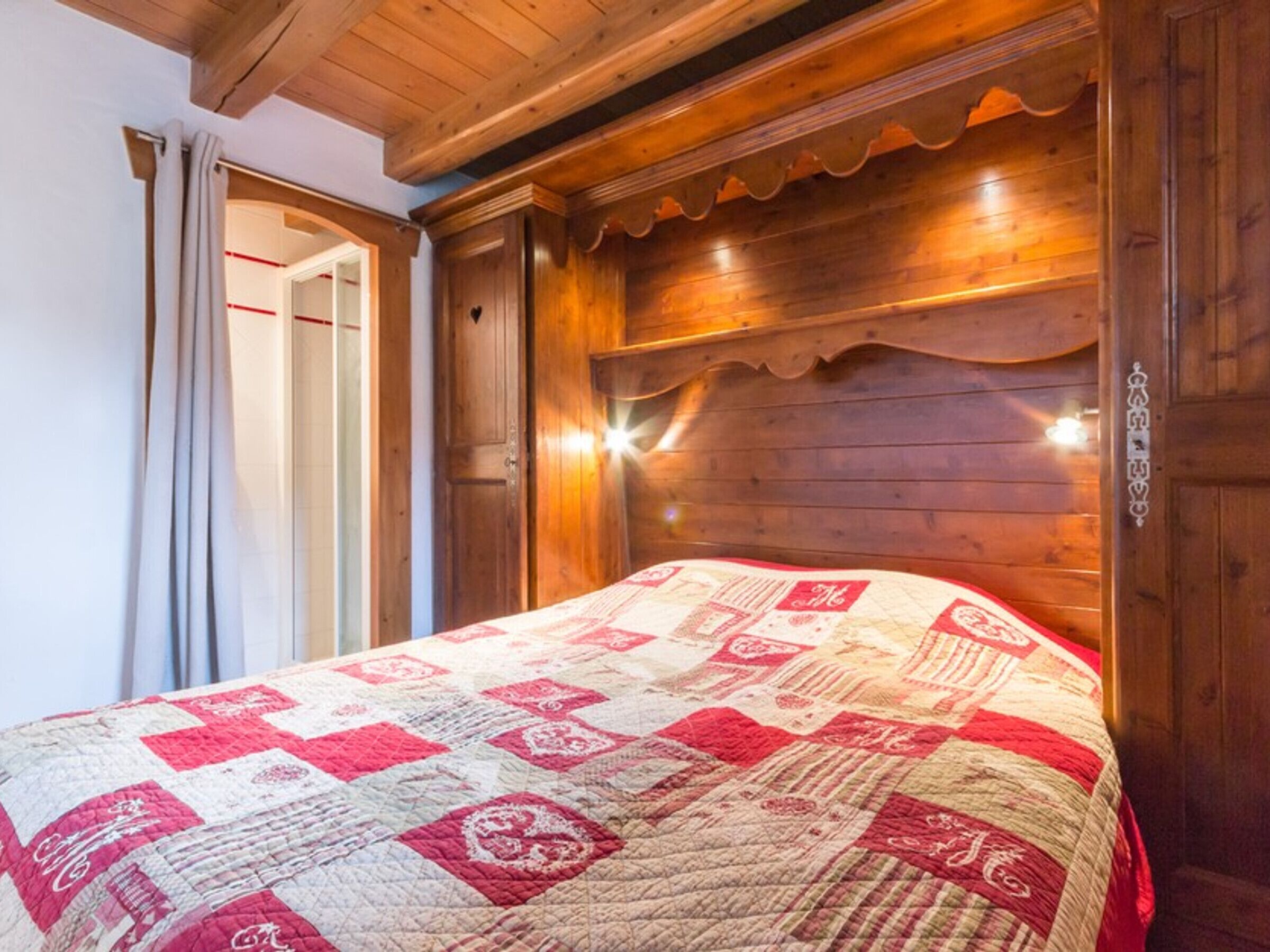 Une chambre à coucher en bois avec une couvre-lit matelassé, une porte dotée d’une poignée et un luminaire placé au-dessus du lit.
