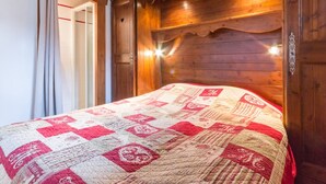 Een houten slaapkamer met een gewatteerde sprei, een deur met een deurklink en een lamp boven het bed.